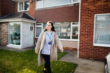 A white female nurse walking outside of a house