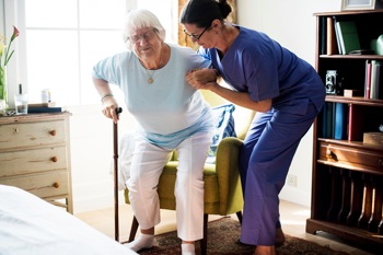 An elderly woman being assisted by a domiciliary care nurse at home.