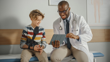 A young boy sitting with a doctor looking at a tablet