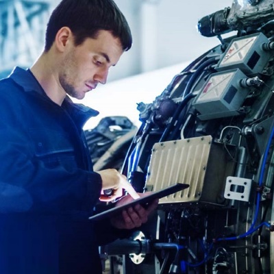 Man using a tablet beside a large industrial machine with control boxes and wiring