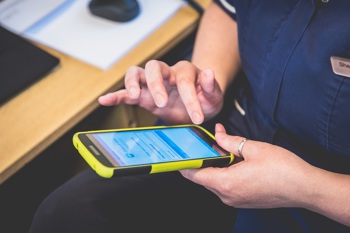 A domiciliary care nurse using care management software on a smartphone.