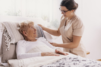 image of a carer looking after a woman in bed to show how addressing the determinants reduces hospital admissions