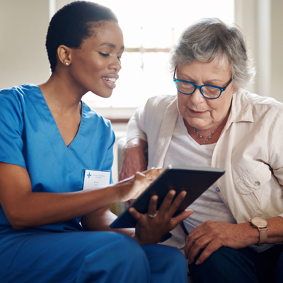 A black nurse showing something to an elderly lady on the tablet