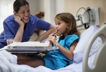 A child in a hospital bed being cared for by a nurse.