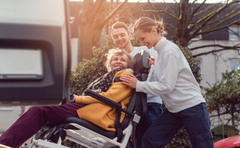 Image of two support workers helping an old age woman in a wheelchair cross the road to show what INTs are