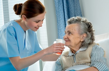 A nurse giving a hospital ward patient a drink whilst in bed.