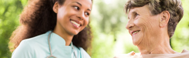 A young female carer smiling at an elderly female who is smiling back at her