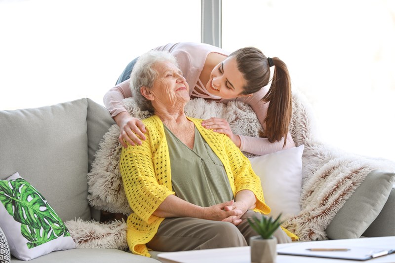 Elderly lady in yellow cardigan being show affection by a young brunette girl