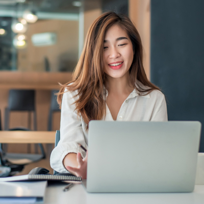 Brown-haired lady in white shirt smiling at laptop