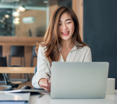 Brown-haired lady in white shirt smiling at laptop