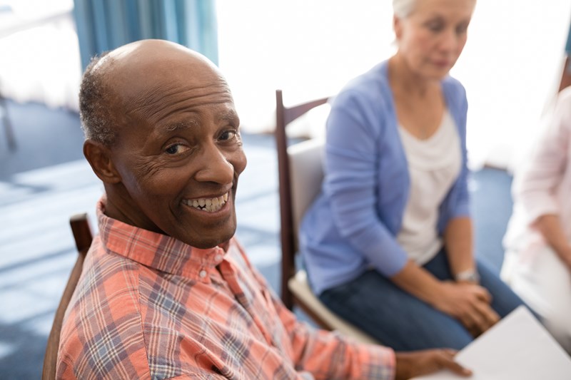 An image of an elderly man smiling within a group of other elderly people