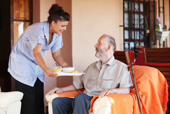 Care worker serving elderly man breakfast following RQIA standards