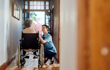An elderly woman on a wheelchair being comforted by a female nurse