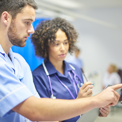 A white male nurse showing something to a black female nurse on a tablet 