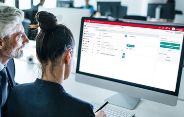 Two professionals collaborating at a computer displaying a red-and-white business software interface